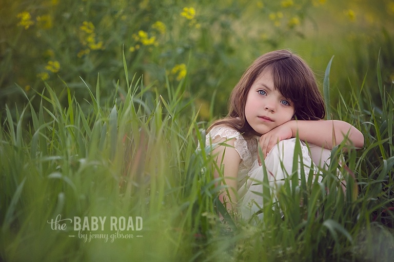 Blue eyed girl sitting in a field of grass and yellow flowers