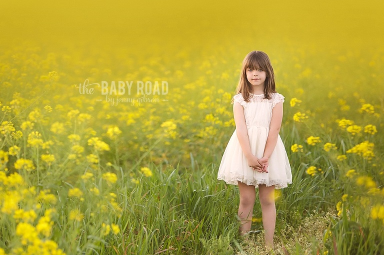 girl in white dress standing in a field of yellow mustard flowers